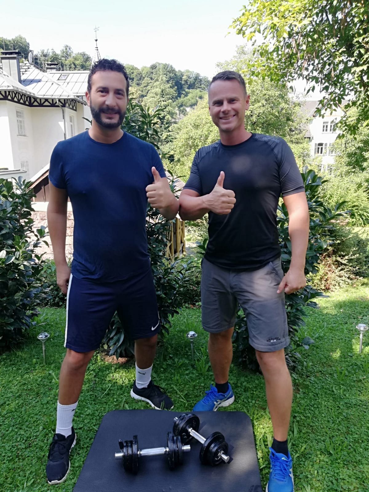 Michael Feneberg mit einem Klienten nach einer Trainingseinheit im
                         Garten, daneben Kurzhanteln auf einer Matte.